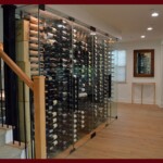 This under-the-stairs wine closet has dual-swing frameless glass wine cellar doors. Glass wine cellar with frameless glass doors at the foot of a staircase
